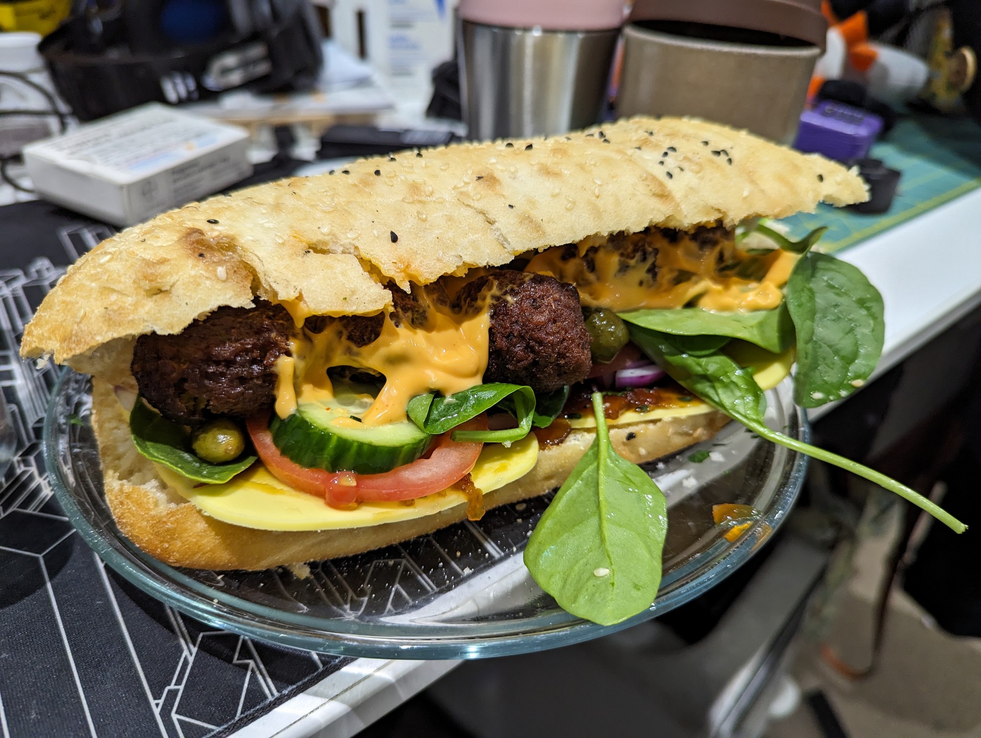 Turkish roll, with falafel balls, tomato, cucumber, pickles, vegan cheese, sriracha mayo sauce, tomato chutney, spinach, red onion and parsley