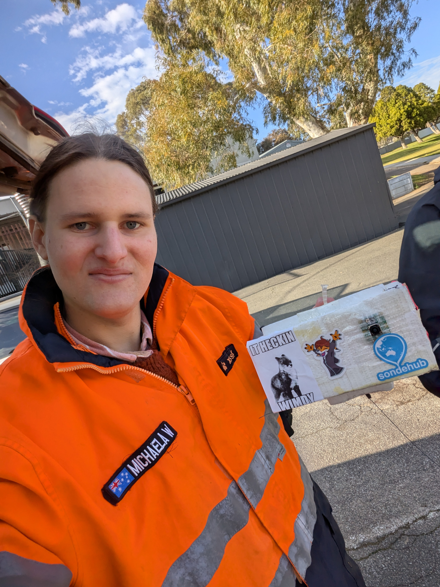 Selfie with me and the payload. The payload has a SondeHub sticker, a its heckin windy sticker and a xssfox sticker