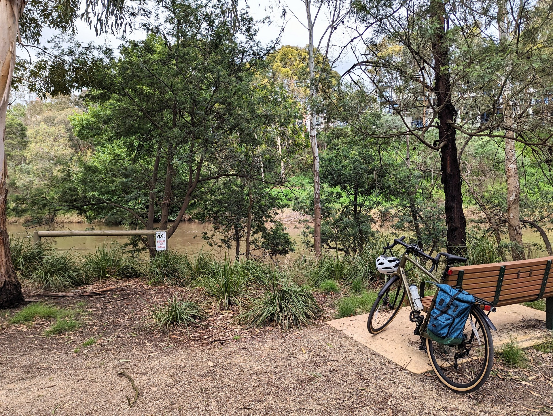 Olive green bike with backpack pannier resting against park bench overlooking the yarra river